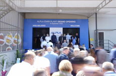 A crowd enters a doorway adorned with a blue banner reading “ALPLA IZMIR PLANT GRAND OPENING September 15, 2026”