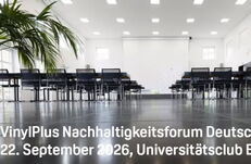 Close-up of a bright, modern seminar room with rows of black chairs and tables, palm trees to the left and right, with a projected white text slide reading ‘VinylPlus Sustainability Forum Germany 22 September 2026, University Club Bonn’
