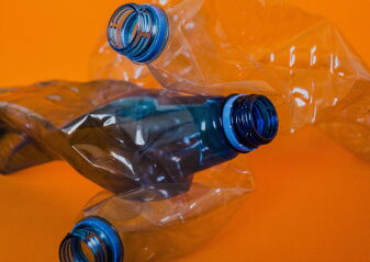 Drei zerdrückte Plastikflaschen mit blauen Verschlüssen vor orangefarbenem Hintergrund