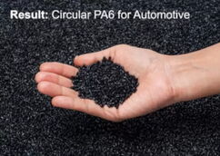 A hand is holding a pile of black polyamide 6 plastic granules on top of a pile of black granules