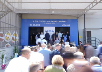 Menschenmenge betritt einen Eingang mit blauem Banner, auf dem 'ALPLA IZMIR PLANT GRAND OPENING 15 September 2026' steht