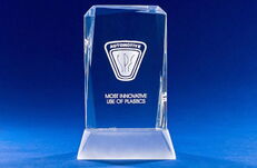 Kristallglas-Trophäe mit eingraviertem Automobil-Logo und der Aufschrift 'MOST INNOVATIVE USE OF PLASTICS' vor blauem Hintergrund