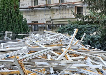 Haufen aus zerlegten weißen Fensterrahmen vor einem mehrstöckigen Gebäude